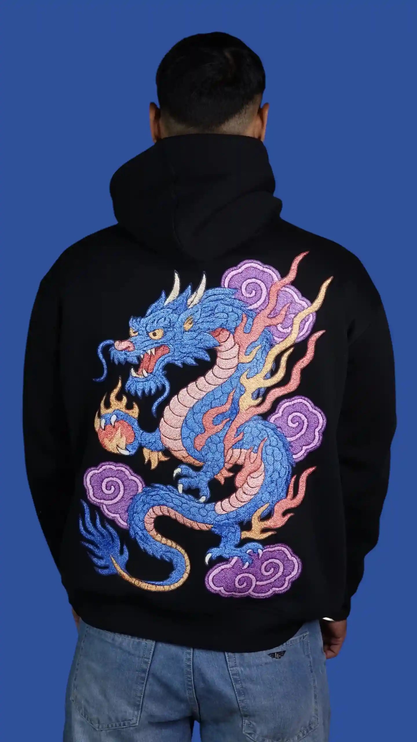 Person wearing a black hoodie with a colorful dragon design on the back against a blue background