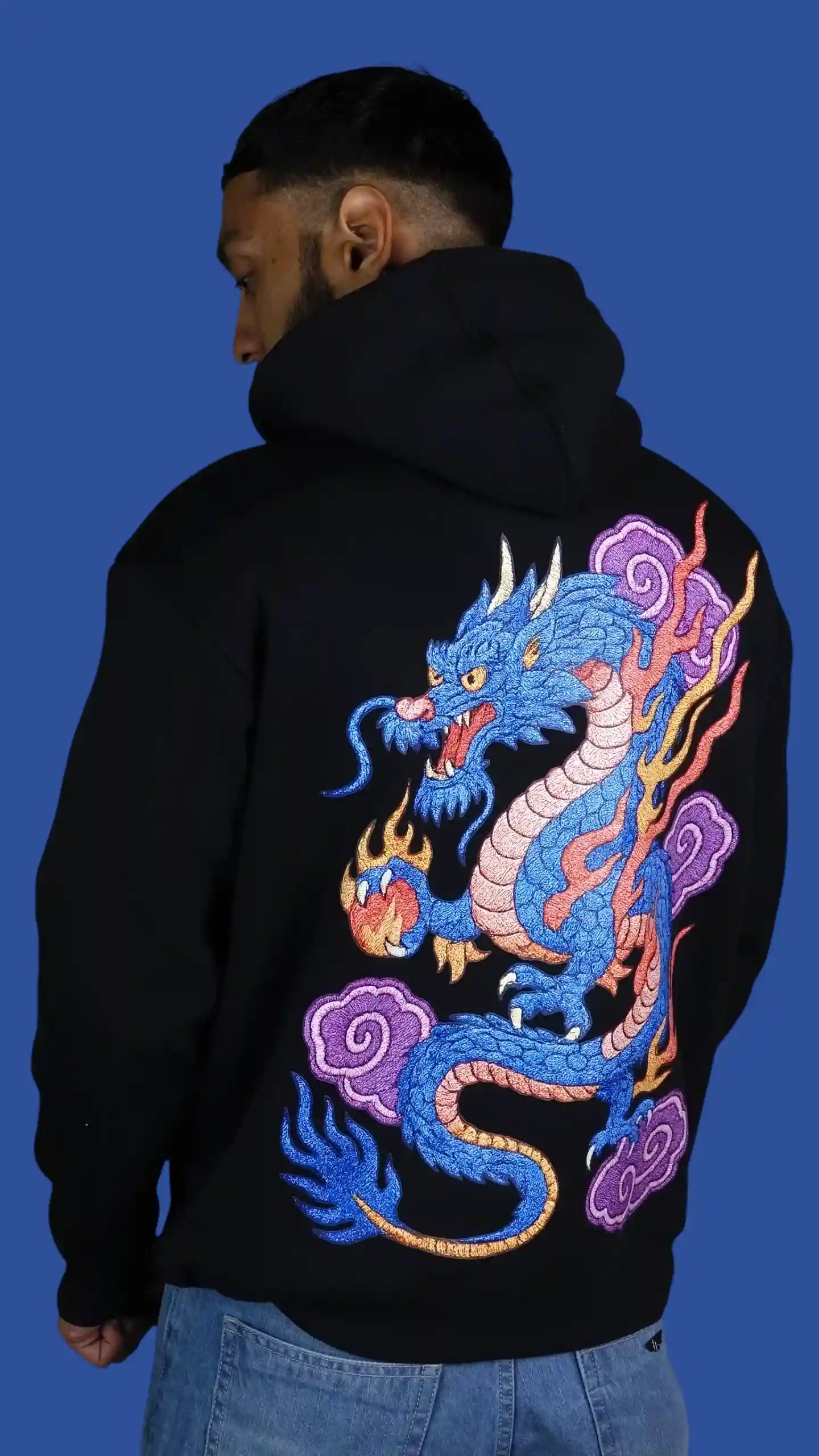 Person wearing a black hoodie with a colorful dragon design on the back against a blue background
