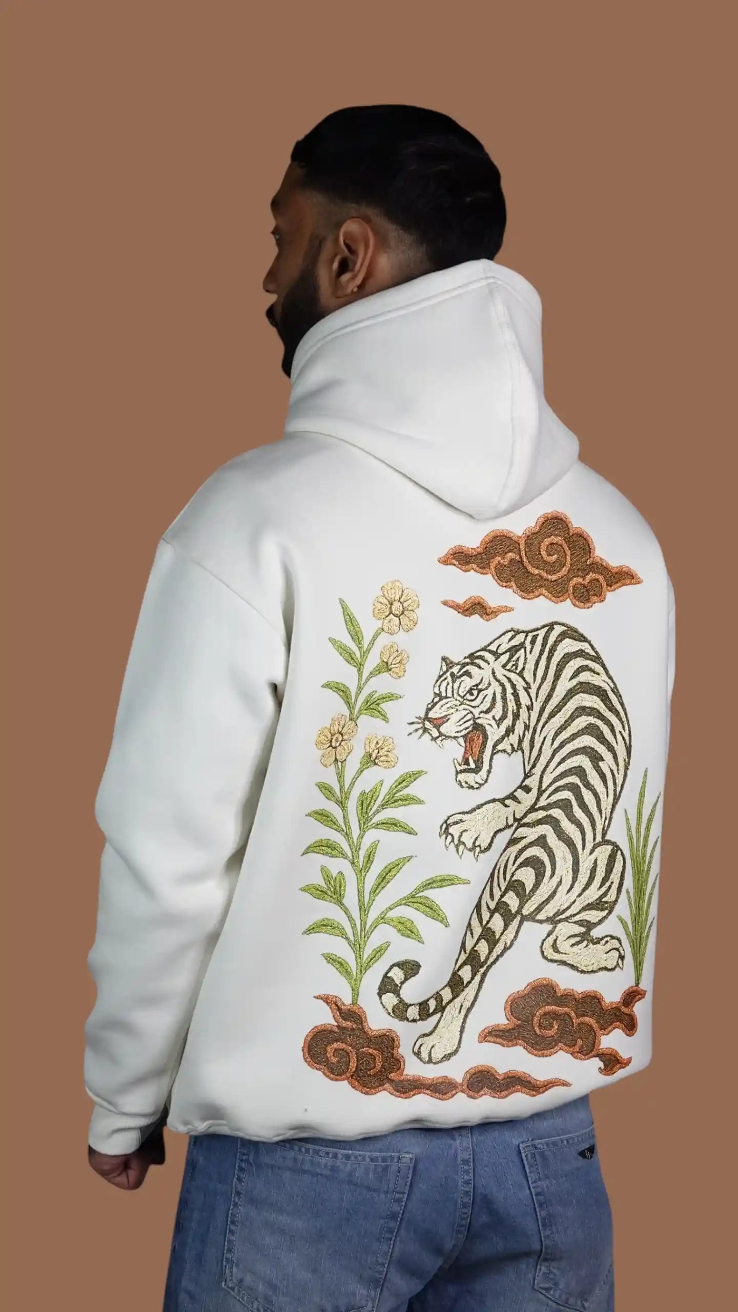 Person wearing a white hoodie with a tiger design on the back against a brown background