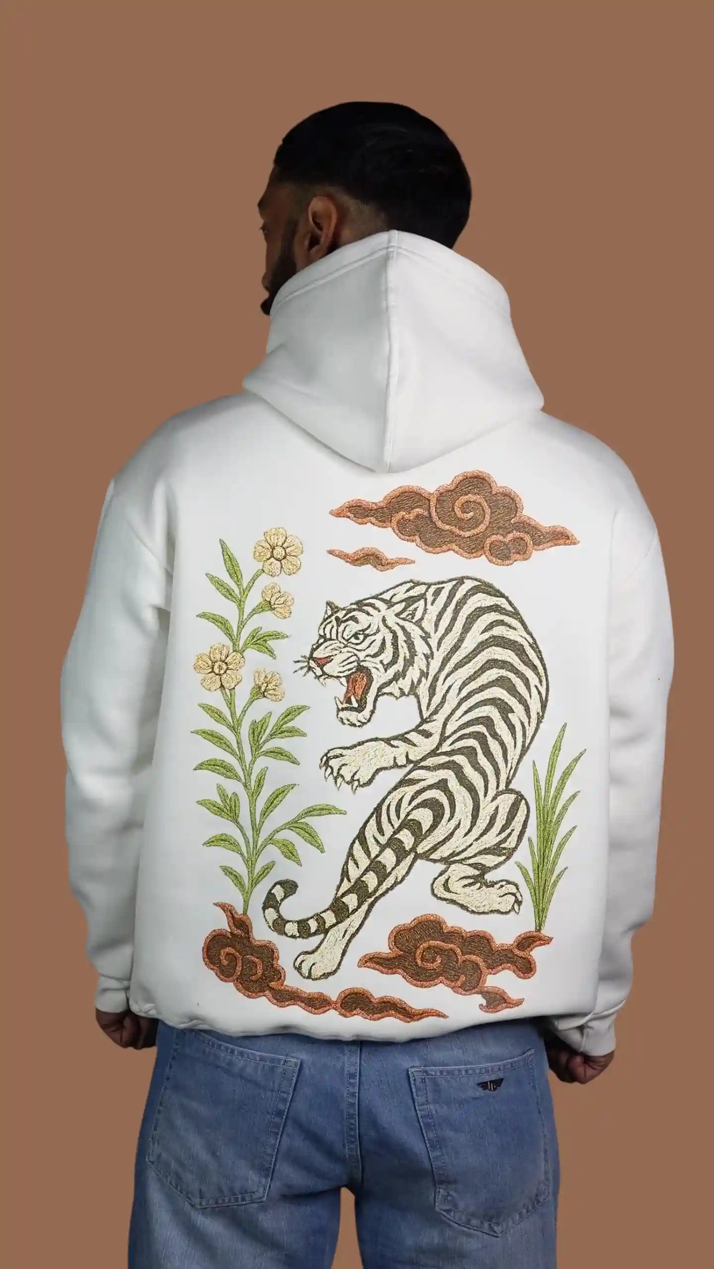 Person wearing a white hoodie with a tiger design on the back against a brown background